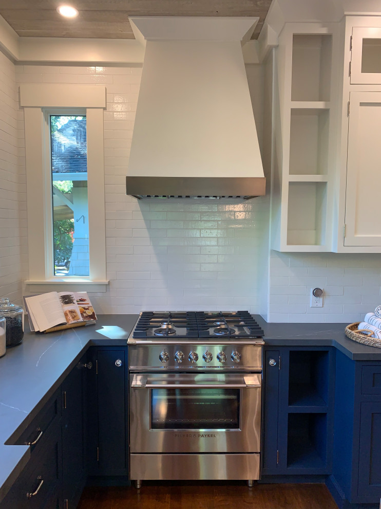 Photo of a large arts and crafts u-shaped eat-in kitchen in San Francisco with an undermount sink, beaded inset cabinets, blue cabinets, quartz benchtops, white splashback, brick splashback, stainless steel appliances, medium hardwood floors, with island, brown floor, black benchtop and timber.