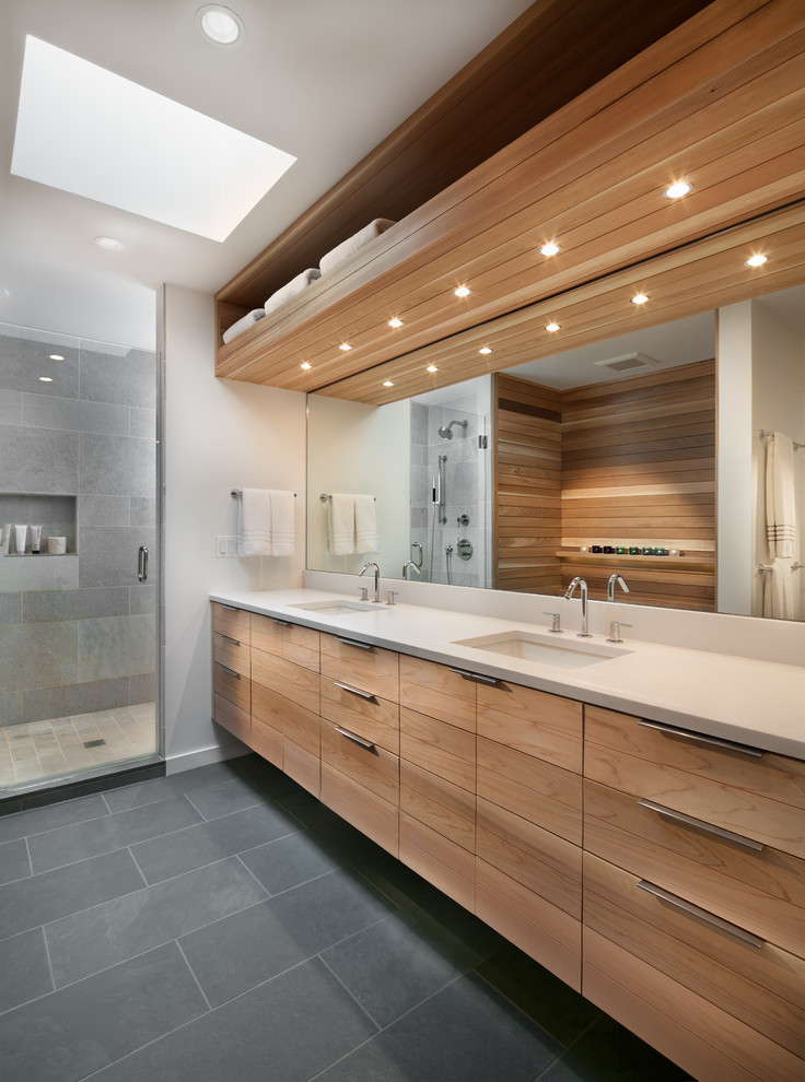 This is an example of a contemporary bathroom in DC Metro with flat-panel cabinets, medium wood cabinets, an alcove shower, gray tile, white walls, an undermount sink, grey floor, a hinged shower door and white benchtops.