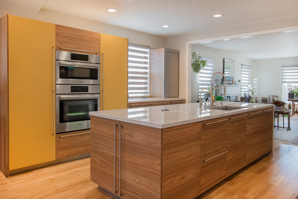 Photo of a mid-sized modern u-shaped eat-in kitchen in Los Angeles with a drop-in sink, flat-panel cabinets, brown cabinets, quartzite benchtops, white splashback, porcelain splashback, stainless steel appliances, laminate floors, with island, brown floor and white benchtop.