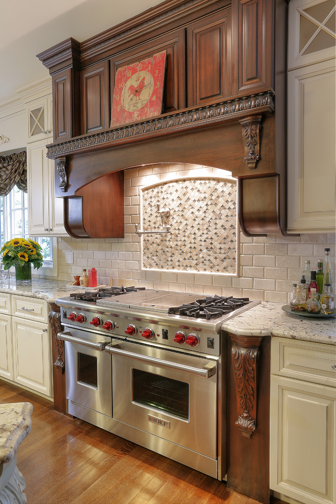 Photo of a country u-shaped separate kitchen in New York with raised-panel cabinets, granite benchtops, stone tile splashback, medium hardwood floors, white cabinets, beige splashback, stainless steel appliances, with island and grey benchtop.
