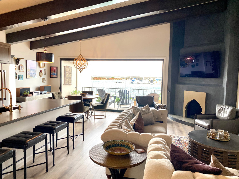 Inspiration for a mid-sized eclectic open concept living room in Orange County with vinyl floors, a corner fireplace, a plaster fireplace surround, a wall-mounted tv, brown floor and exposed beam.
