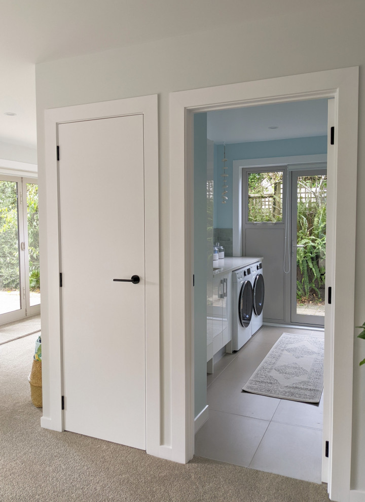 Photo of a beach style single-wall dedicated laundry room in Auckland with an undermount sink, cement tile splashback, blue walls, porcelain floors, a side-by-side washer and dryer, grey floor and white benchtop.