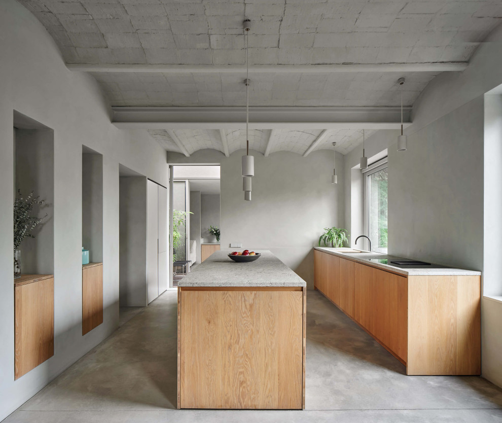 Cette image montre une cuisine parallèle design en bois clair avec un évier encastré, un placard à porte plane, sol en béton ciré, îlot, un sol gris et un plan de travail gris.