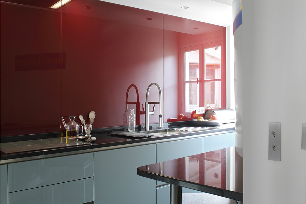 Photo of a small midcentury l-shaped open plan kitchen in Paris with an undermount sink, flat-panel cabinets, blue cabinets, granite benchtops, red splashback, glass sheet splashback, stainless steel appliances, marble floors and no island.