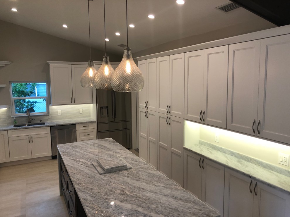 Kitchen - mid-sized transitional u-shaped beige floor kitchen idea in Miami with an undermount sink, recessed-panel cabinets, white cabinets, gray backsplash, glass tile backsplash, stainless steel appliances, an island and gray countertops