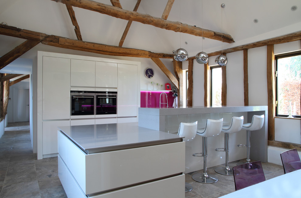 Contemporary galley kitchen in Hertfordshire with with island, flat-panel cabinets, white cabinets, pink splashback, glass sheet splashback, stainless steel appliances, grey floor and grey benchtop.
