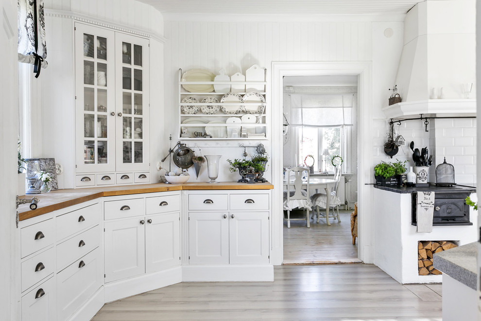 Photo of a traditional separate kitchen in Other with glass-front cabinets, white cabinets, wood benchtops, white splashback, subway tile splashback and beige floor.