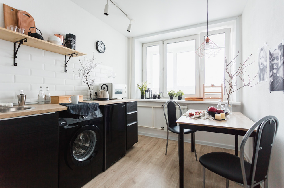 Inspiration for a scandinavian l-shaped separate kitchen in Malaga with a drop-in sink, flat-panel cabinets, black cabinets, white splashback, subway tile splashback, black appliances, light hardwood floors and no island.