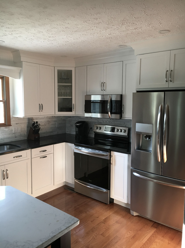 Inspiration for a large transitional single-wall medium tone wood floor eat-in kitchen remodel with an undermount sink, shaker cabinets, white cabinets, granite countertops, multicolored backsplash, marble backsplash, stainless steel appliances, an island and black countertops