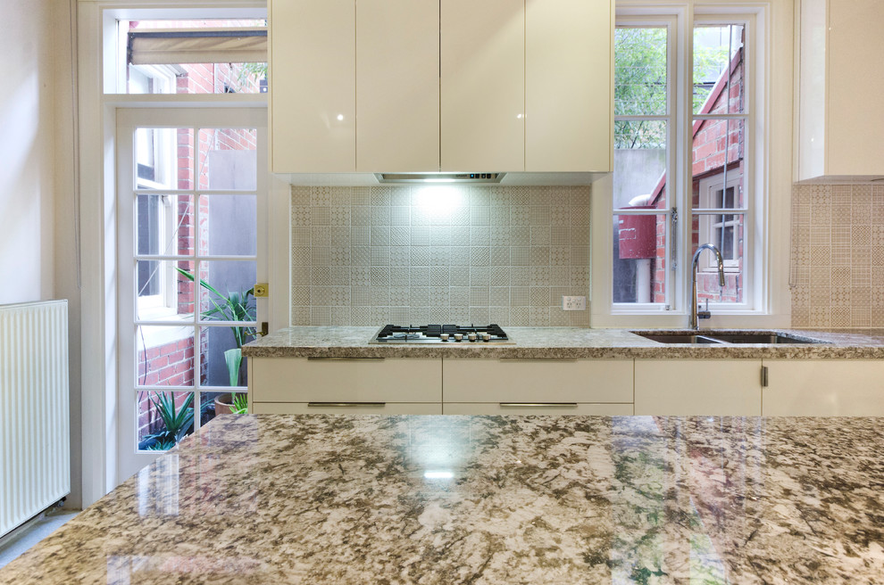 This is an example of a mid-sized contemporary galley separate kitchen in Melbourne with an undermount sink, flat-panel cabinets, beige cabinets, granite benchtops, beige splashback, ceramic splashback, stainless steel appliances, porcelain floors, with island and beige floor.