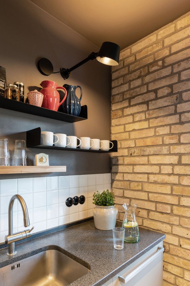 Inspiration for a small industrial galley open plan kitchen in Bremen with an undermount sink, flat-panel cabinets, grey cabinets, granite benchtops, white splashback, ceramic splashback, stainless steel appliances, light hardwood floors, with island, brown floor and black benchtop.