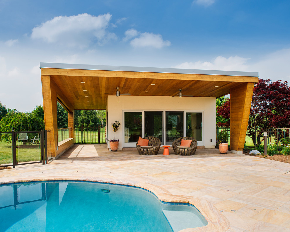 Photo of a large contemporary backyard kidney-shaped pool in Philadelphia with a pool house and natural stone pavers.