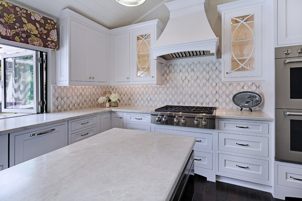 Mid-sized transitional u-shaped dark wood floor enclosed kitchen photo in Orange County with a farmhouse sink, beaded inset cabinets, white cabinets, quartzite countertops, white backsplash, glass sheet backsplash, stainless steel appliances and an island