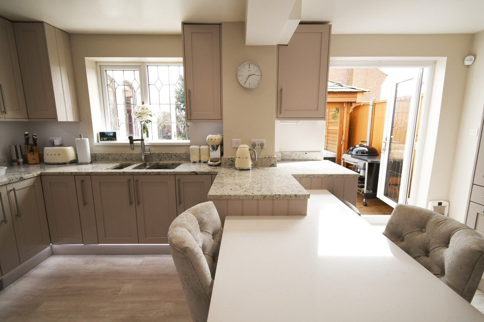Photo of a medium sized classic l-shaped enclosed kitchen in Essex with a double-bowl sink, shaker cabinets, all types of cabinet finish, granite worktops, grey splashback, metal splashback, black appliances, laminate floors, a breakfast bar, white worktops and feature lighting.