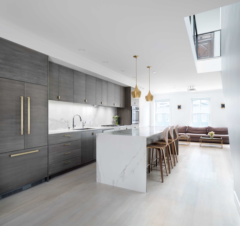 Mid-sized modern galley open plan kitchen in New York with a single-bowl sink, flat-panel cabinets, medium wood cabinets, solid surface benchtops, white splashback, stone slab splashback, panelled appliances, light hardwood floors, with island and white floor.