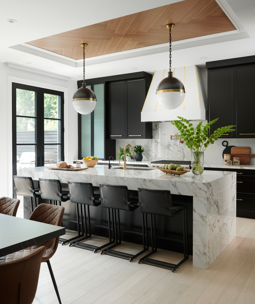 Photo of a large contemporary l-shaped open plan kitchen in Toronto with a double-bowl sink, shaker cabinets, black cabinets, marble benchtops, white splashback, marble splashback, panelled appliances, light hardwood floors, with island, white benchtop and recessed.