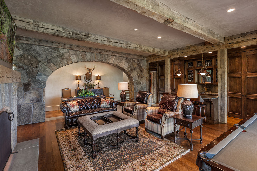 Large mediterranean open concept family room in Other with grey walls, medium hardwood floors, a standard fireplace, a stone fireplace surround, a wall-mounted tv and brown floor.