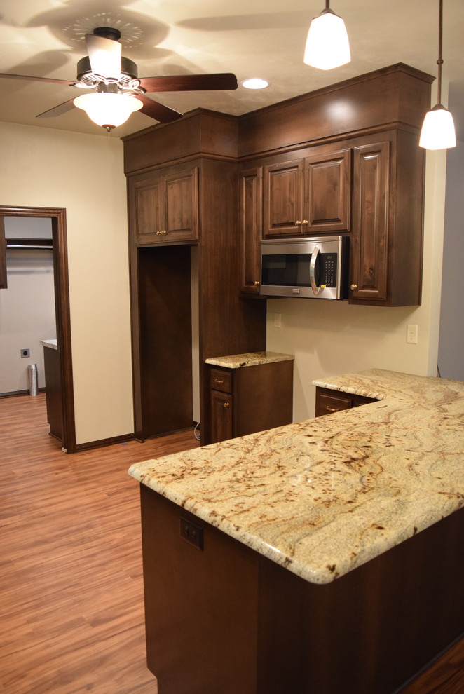 Light wood floor open concept kitchen photo with an undermount sink, raised-panel cabinets, dark wood cabinets, granite countertops, white backsplash, ceramic backsplash, stainless steel appliances and a peninsula