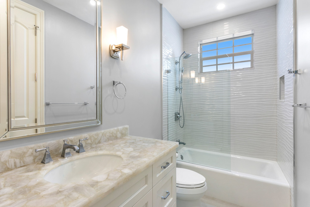 Exempel på ett stort klassiskt flerfärgad flerfärgat badrum för barn, med luckor med upphöjd panel, grå skåp, ett hörnbadkar, en dusch i en alkov, en toalettstol med separat cisternkåpa, vit kakel, marmorkakel, grå väggar, klinkergolv i porslin, ett undermonterad handfat, bänkskiva i kvartsit, grått golv och med dusch som är öppen