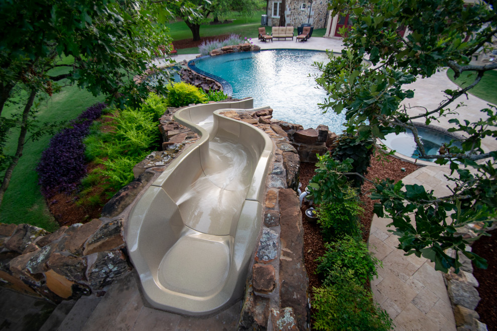 Large country backyard custom-shaped natural pool in Dallas with a water slide and natural stone pavers.