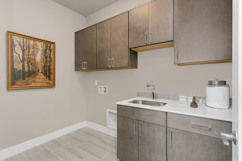 Design ideas for a mid-sized contemporary single-wall dedicated laundry room in Seattle with an utility sink, flat-panel cabinets, medium wood cabinets, quartz benchtops, grey walls, porcelain floors and a side-by-side washer and dryer.