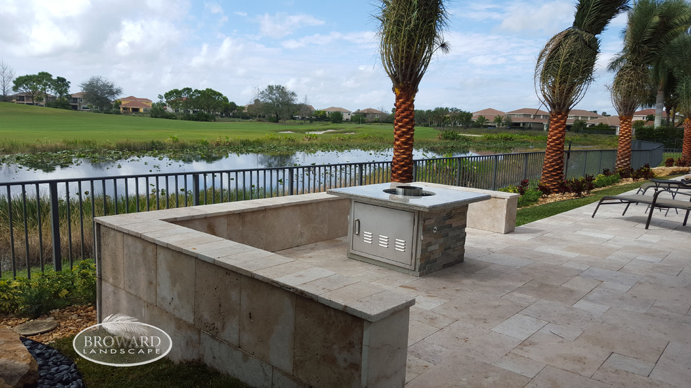 This is an example of a mid-sized contemporary backyard verandah in Miami with a fire feature, natural stone pavers and a pergola.