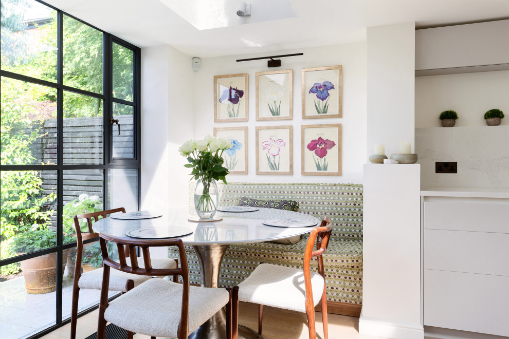 This is an example of a contemporary dining room in London with banquette seating, white walls, light hardwood flooring, beige floors and no fireplace.