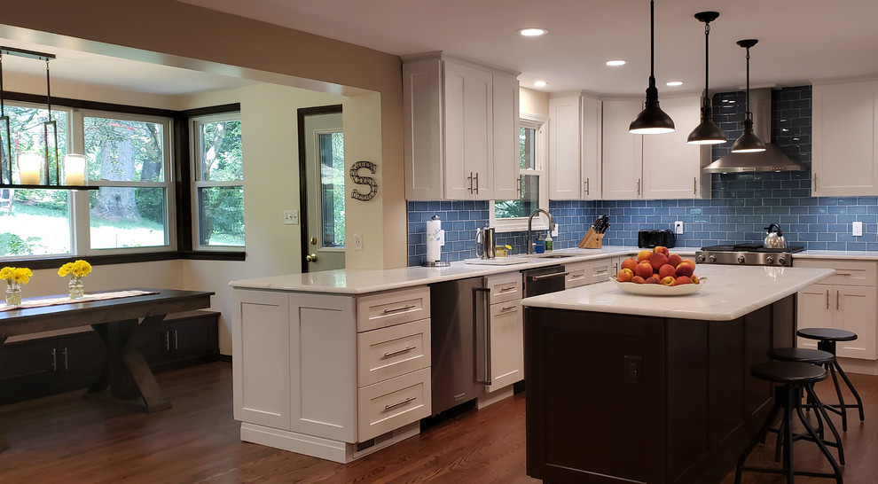 Large transitional u-shaped medium tone wood floor eat-in kitchen photo with shaker cabinets, white cabinets, quartzite countertops, blue backsplash, glass tile backsplash, stainless steel appliances, an island and white countertops