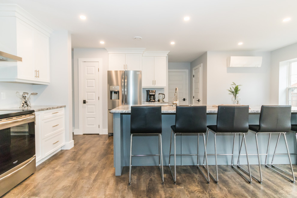 Kitchen - mid-sized l-shaped brown floor and vinyl floor kitchen idea with white cabinets, stainless steel appliances, an island, multicolored countertops, a drop-in sink, recessed-panel cabinets and laminate countertops