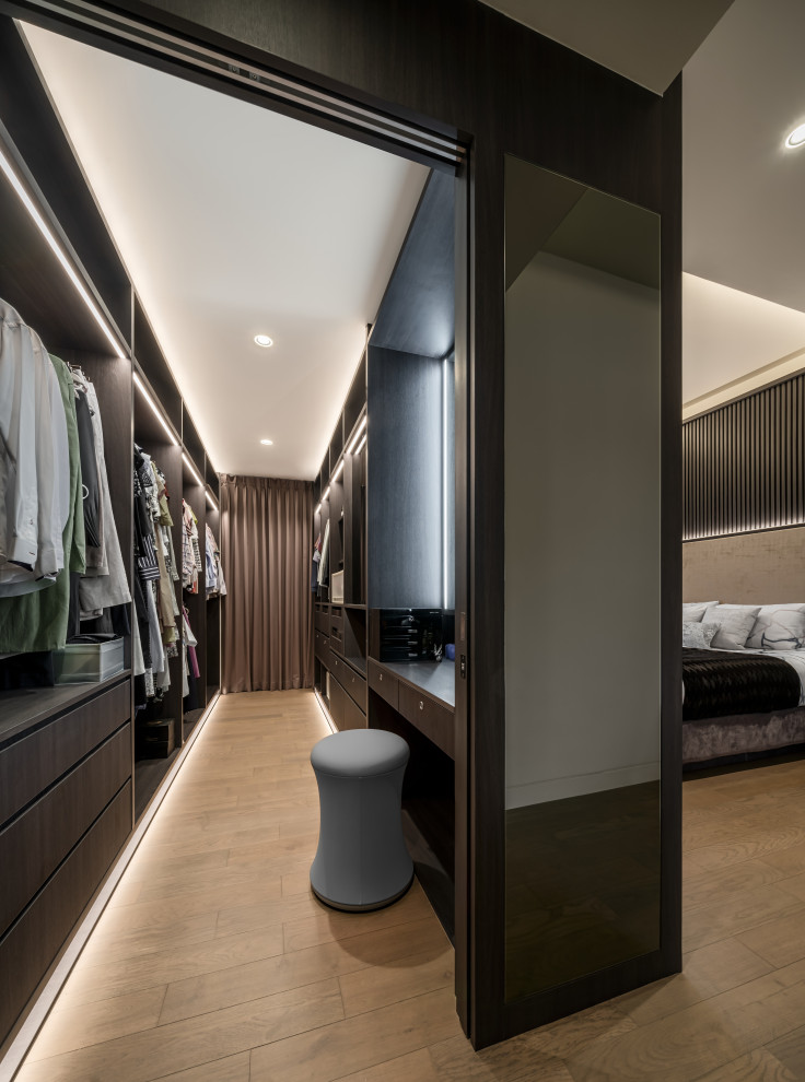 Photo of a large contemporary gender-neutral dressing room in Singapore with flat-panel cabinets, dark wood cabinets and beige floor.