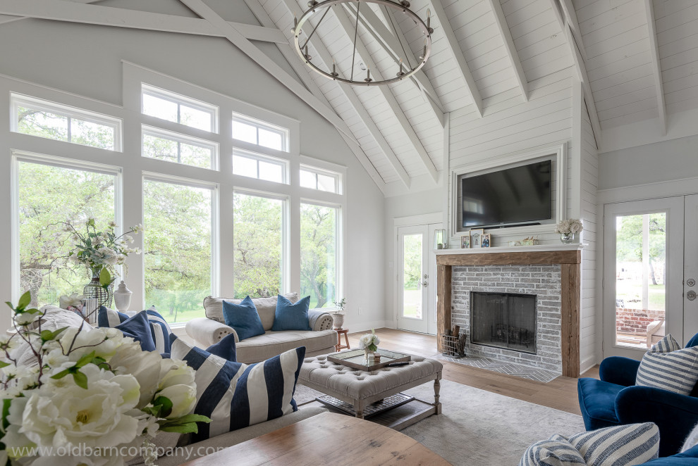 Cette photo montre une grande salle de séjour nature avec un mur blanc, parquet clair, une cheminée standard, un manteau de cheminée en carrelage, un téléviseur fixé au mur, un plafond voûté et du lambris de bois.