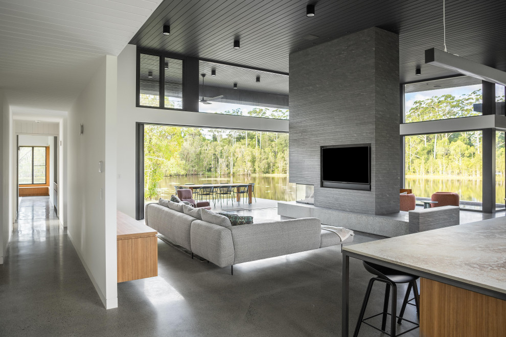 This is an example of a modern open concept living room in Sunshine Coast with concrete floors, a two-sided fireplace, a concrete fireplace surround and a built-in media wall.