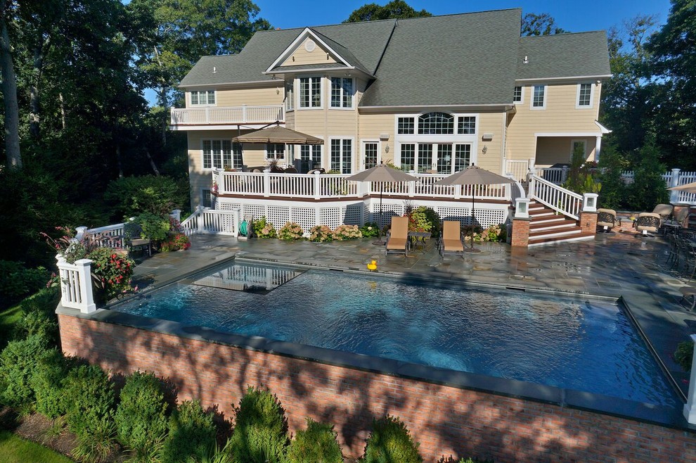 This is an example of a mid-sized traditional backyard l-shaped lap pool in Other with a hot tub and natural stone pavers.