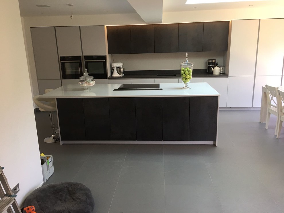 Contemporary single-wall open plan kitchen in London with a drop-in sink, flat-panel cabinets, grey cabinets, quartzite benchtops, black appliances, porcelain floors, with island and grey floor.