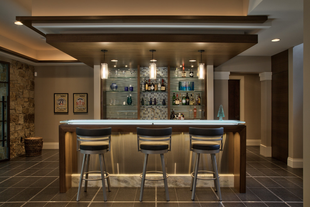 Photo of a large contemporary single-wall seated home bar in Minneapolis with flat-panel cabinets, medium wood cabinets, glass benchtops, blue splashback, glass tile splashback, porcelain floors, grey floor and blue benchtop.
