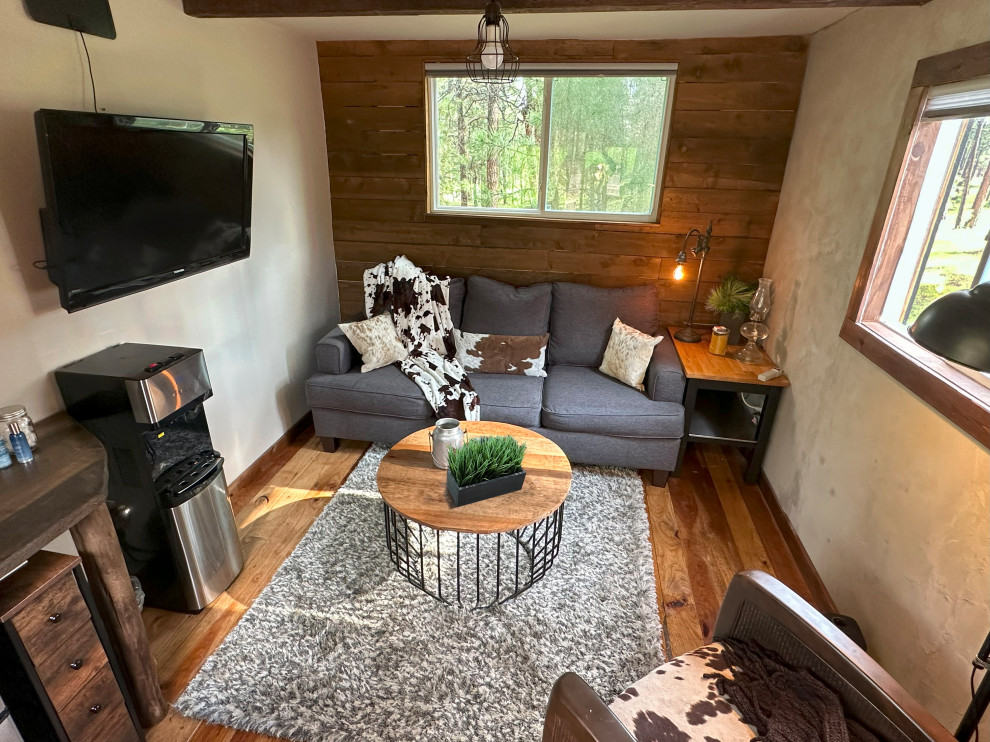 Aménagement d'une petite salle de séjour en bois avec un mur marron, parquet foncé, un téléviseur fixé au mur et poutres apparentes.