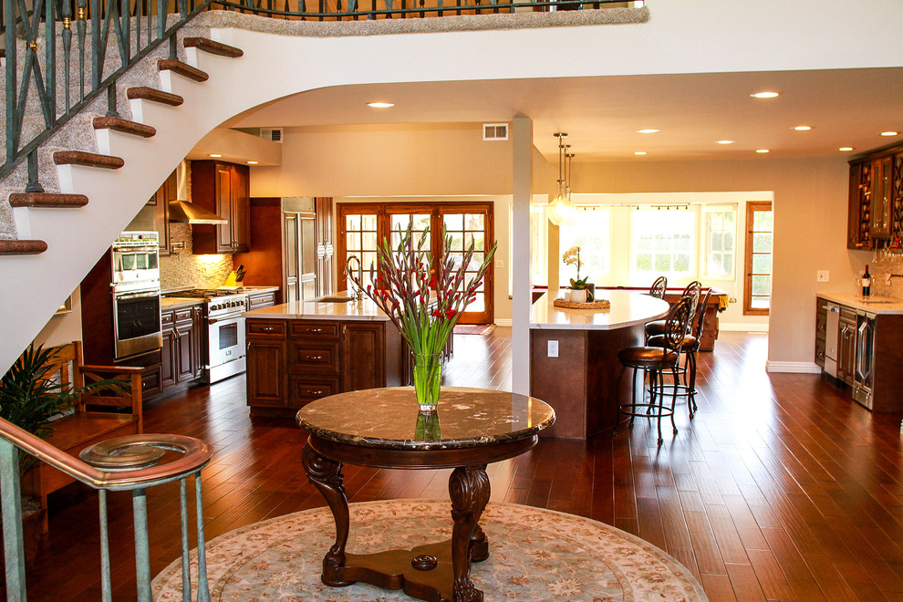 Inspiration for a large transitional medium tone wood floor and brown floor kitchen remodel in Orange County with a double-bowl sink, raised-panel cabinets, brown cabinets, quartzite countertops, white backsplash, stone tile backsplash, stainless steel appliances and two islands