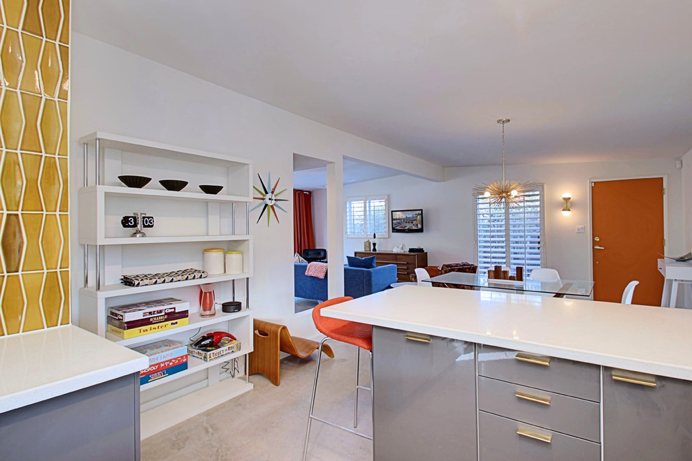 Photo of a mid-sized midcentury l-shaped open plan kitchen in Phoenix with an undermount sink, flat-panel cabinets, grey cabinets, quartz benchtops, yellow splashback, ceramic splashback, stainless steel appliances, concrete floors and a peninsula.