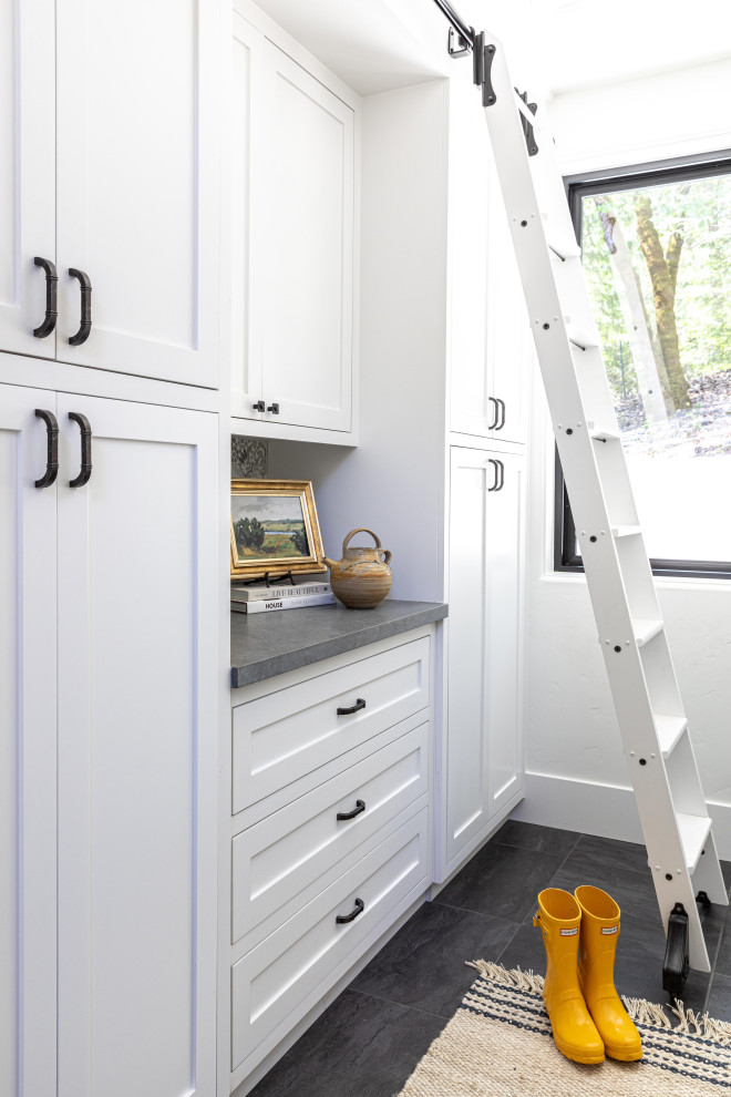 This is an example of a mid-sized country u-shaped laundry cupboard in Sacramento with a farmhouse sink, shaker cabinets, white cabinets, quartz benchtops, multi-coloured splashback, ceramic splashback, white walls, porcelain floors, a side-by-side washer and dryer, grey floor and grey benchtop.