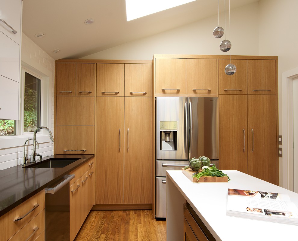 This is an example of a small modern l-shaped separate kitchen in Seattle with a single-bowl sink, flat-panel cabinets, light wood cabinets, quartz benchtops, white splashback, ceramic splashback, stainless steel appliances, light hardwood floors, with island and brown floor.