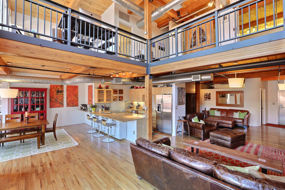 This is an example of an industrial open concept living room in Denver with white walls and medium hardwood floors.