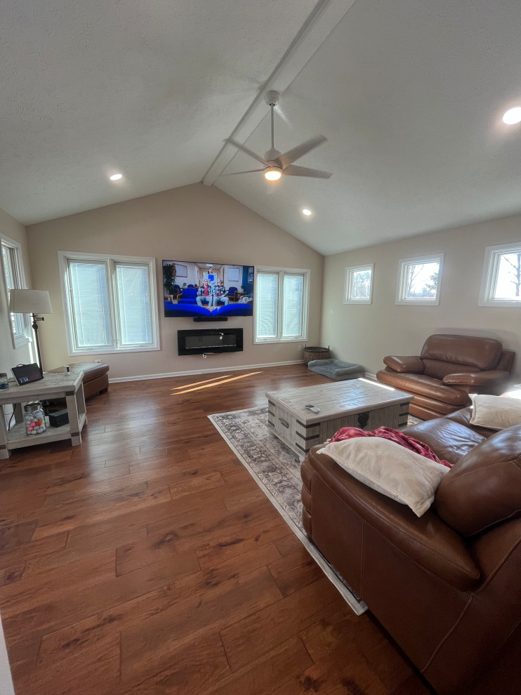 Example of a large farmhouse open concept medium tone wood floor, beige floor and vaulted ceiling family room design in Indianapolis with beige walls, a hanging fireplace, a shiplap fireplace and a wall-mounted tv