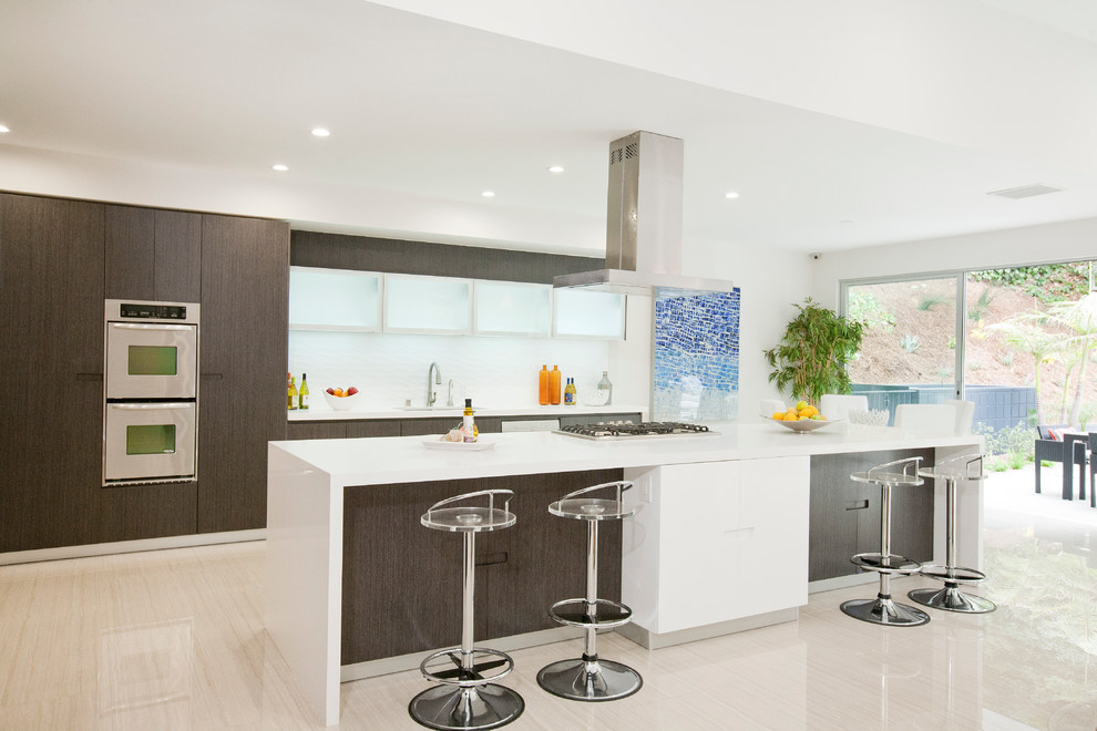 Contemporary galley kitchen in Los Angeles with flat-panel cabinets, dark wood cabinets, white splashback and with island.