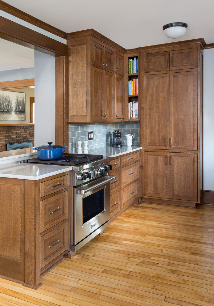 Photo of a mid-sized arts and crafts galley eat-in kitchen in Minneapolis with an undermount sink, flat-panel cabinets, medium wood cabinets, quartz benchtops, blue splashback, ceramic splashback, stainless steel appliances, light hardwood floors, no island and brown floor.