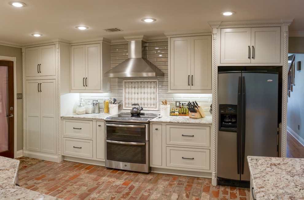Design ideas for a mid-sized transitional l-shaped eat-in kitchen in New Orleans with a farmhouse sink, beaded inset cabinets, white cabinets, granite benchtops, subway tile splashback, stainless steel appliances, brick floors, a peninsula and green splashback.