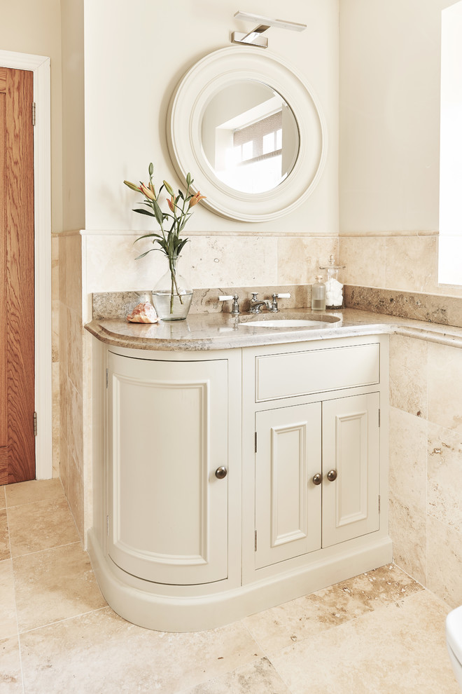 This is an example of a traditional powder room in Wiltshire with recessed-panel cabinets, beige cabinets, beige tile, beige walls, an undermount sink, beige floor and beige benchtops.