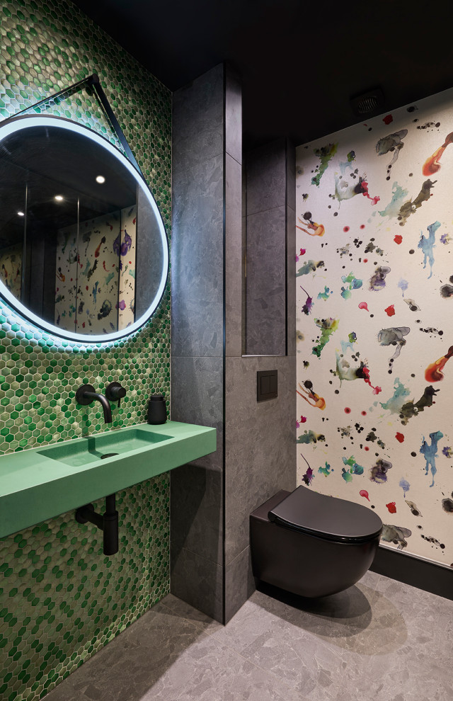 This is an example of a contemporary family bathroom in London with a wall mounted toilet, green tiles, mosaic tiles, multi-coloured walls, porcelain flooring, a wall-mounted sink, concrete worktops, grey floors, green worktops, a feature wall, a single sink and wallpapered walls.