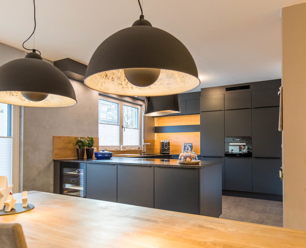 Mid-sized contemporary u-shaped eat-in kitchen in Nuremberg with black cabinets, granite benchtops, a peninsula, an integrated sink, flat-panel cabinets, brown splashback, timber splashback, black appliances and brown floor.