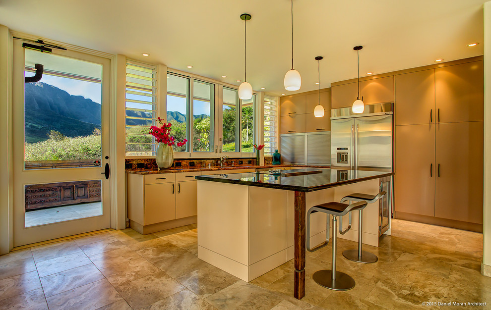 This is an example of a tropical kitchen in Hawaii with a single-bowl sink, flat-panel cabinets, beige cabinets, granite benchtops, multi-coloured splashback, stone slab splashback, stainless steel appliances, travertine floors and with island.