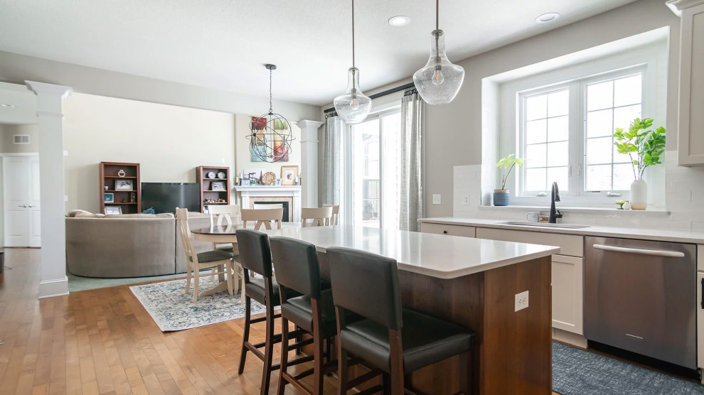 Eat-in kitchen - large transitional u-shaped medium tone wood floor and brown floor eat-in kitchen idea in Minneapolis with a single-bowl sink, shaker cabinets, white cabinets, quartz countertops, white backsplash, porcelain backsplash, stainless steel appliances, an island and white countertops